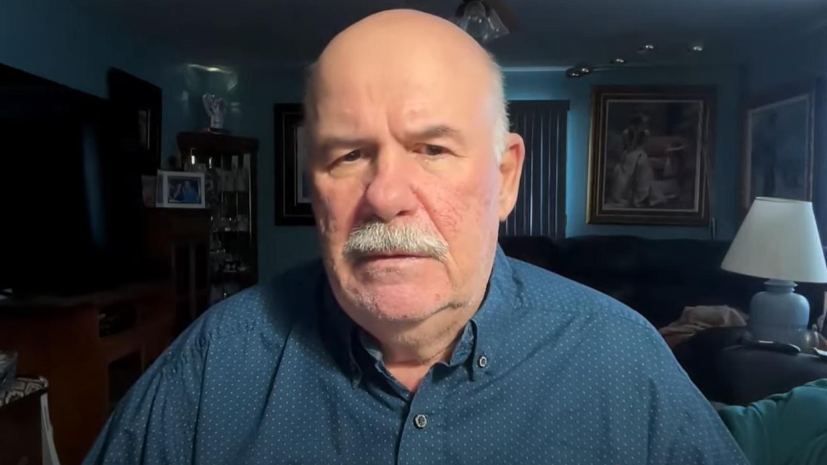 Man in his 60s with white hair and white mustache wearing a blue button-up shirt.